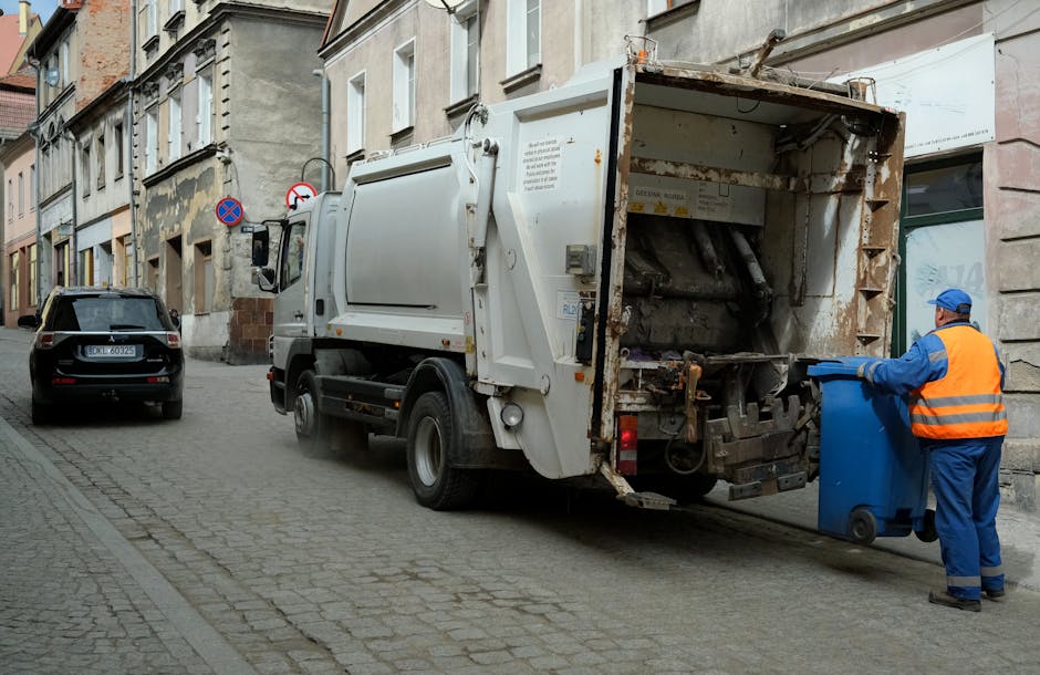 A person's hand and forearm, extending from the left side of the image, holding a green plastic rubbish bag that appears to contain general waste. The bag is gathered at the top with a twist tie or kn